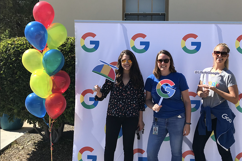 Three students with Google backdrop and balloons